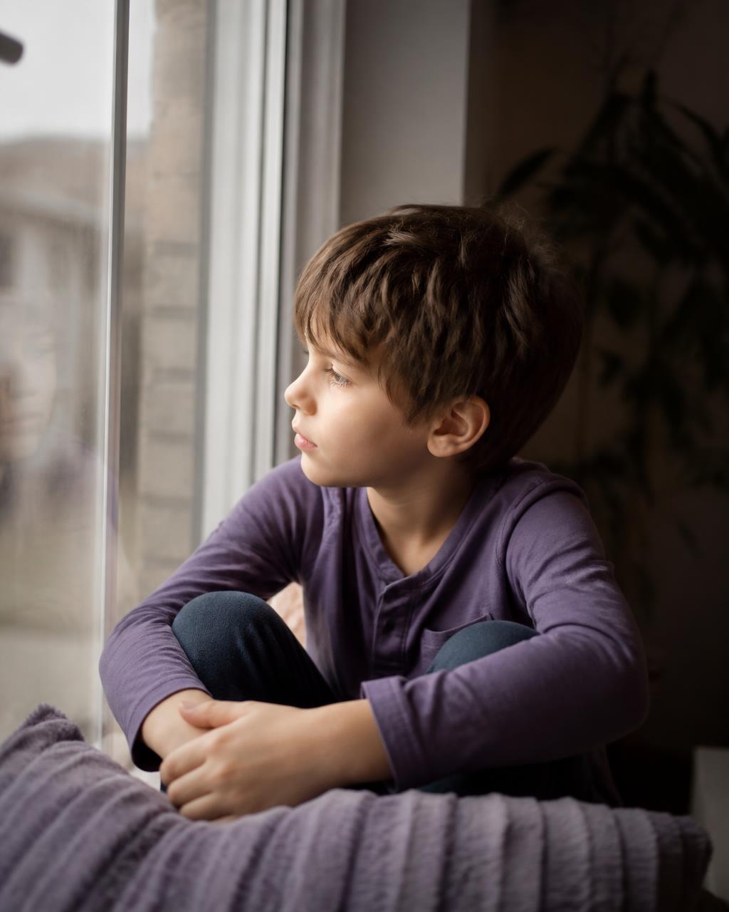A thoughtful young boy sitting quietly by a window in soft daylight